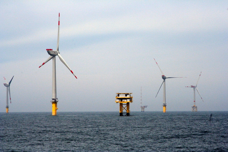 Some wind turbines out in the ocean. There is no land in sight, and it is a little foggy.